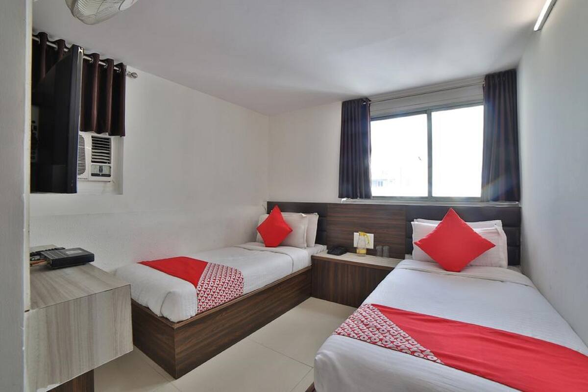 A hotel room with two beds, a small desk, a window with curtains, and a ceiling fan.