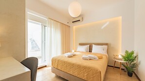 Camera d'albergo con un letto, una scrivania, una sedia, una pianta in vaso e vista sull'esterno.