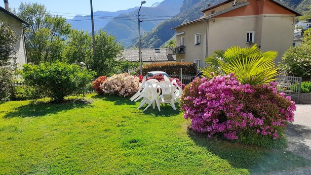 Un jardín bien cuidado con diversos arbustos y flores, un camino pavimentado y un edificio con balcón.
