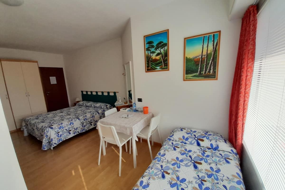 Una habitación con dos camas individuales, una pequeña mesa con sillas, un escritorio y un espejo.