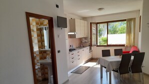 Una cocina compacta con comedor, un televisor montado en la pared y un ventanal con cortinas.