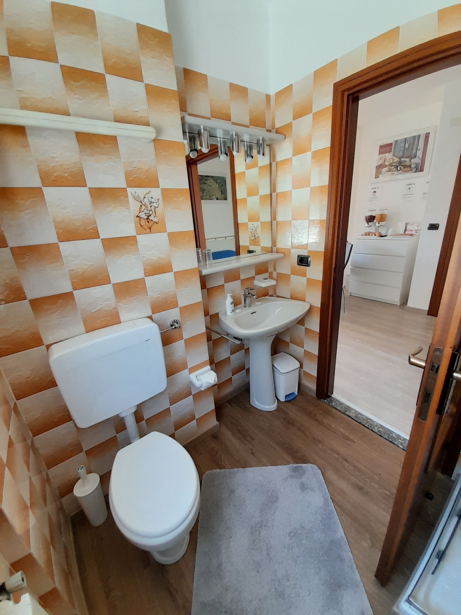 Une salle de bain avec un mur recouvert de carreaux à motifs géométriques, des toilettes, un lavabo et un miroir.