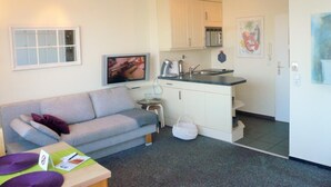 A compact living space with a sofa, a small table, a kitchenette, and a ceiling fan. - App. Grimme 09 O, Germany (Sylt)