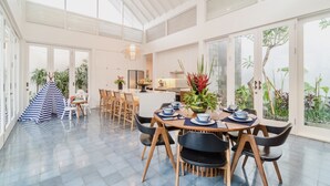 A spacious dining area with a high ceiling, large windows, and a view of greenery outside.