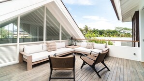 A modern outdoor living space with a white sofa, wicker chairs, and a wooden deck.
