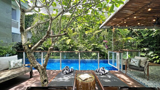 A poolside area with lounge chairs, a wooden table, and a wicker stool.