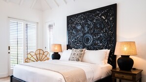 A bedroom with a large bed, two bedside tables with lamps, a decorative headboard, and a door with blinds.