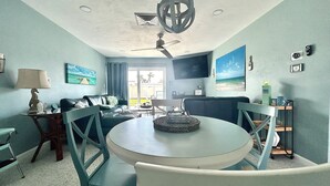 A living room with a round table, chairs, a sofa, a TV, and a ceiling fan.