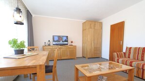 A living room with a wooden dining table, chairs, a sofa, a television, and a wardrobe.