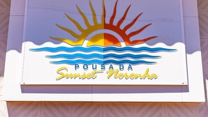 Um letreiro com um sol e ondas, e o texto 'Pousada Sunset Noronha'.