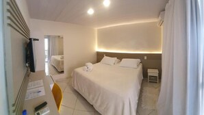 Quarto de hotel com uma cama, mesas de cabeceira, escrivaninha com cadeira, espelho e janela com cortinas.