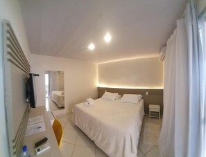 Habitación de hotel con cama, mesitas de noche, escritorio con silla, espejo y ventana con cortinas.