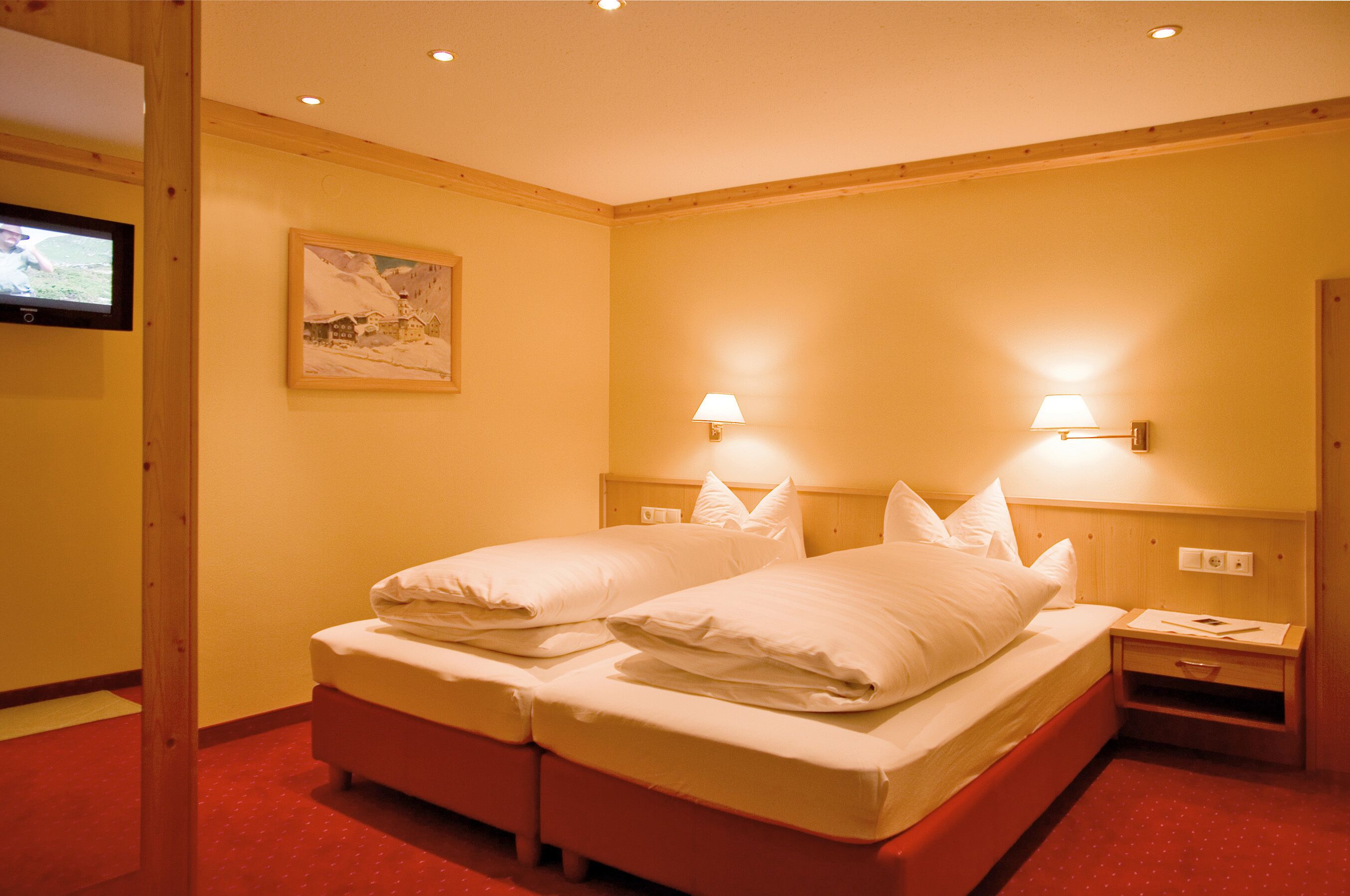 A hotel room with two beds, a television, and two wall-mounted lamps.