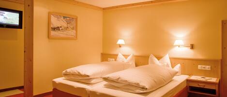 A hotel room with two beds, a television, and two wall-mounted lamps.