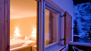 Un dormitorio acogedor con cama, lámparas de noche y ventana con vistas a árboles cubiertos de nieve.