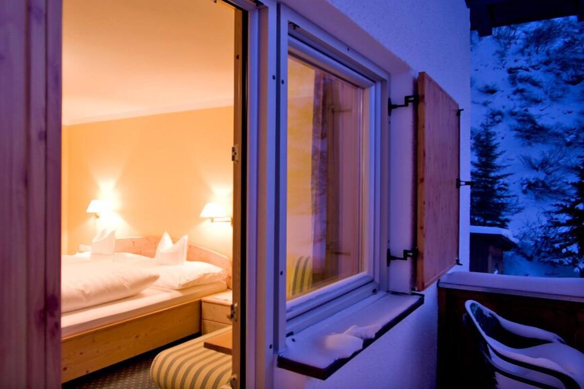 Un dormitorio acogedor con cama, lámparas de noche y ventana con vistas a árboles cubiertos de nieve.