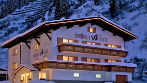 Un edificio de dos pisos con el nombre "landhaus maria" en la fachada, que presenta balcones de madera y un techo cubierto de nieve.