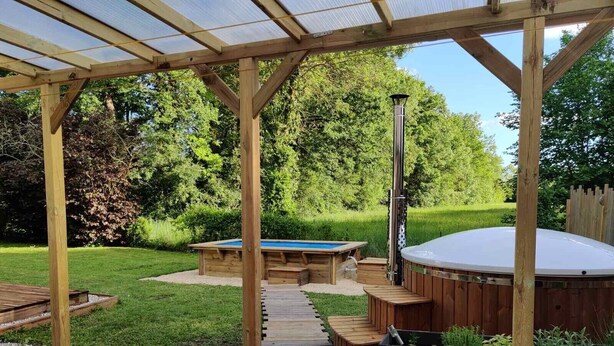 Una terraza de madera con un jacuzzi, mesa de billar y una pérgola.