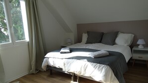 Una cama bien hecha con almohadas y una toalla doblada, una mesita de noche con lámpara y una ventana con cortinas.
