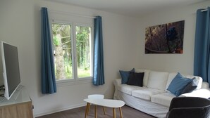 Una sala de estar moderna con un sofá blanco, cojines azules, un sillón negro y un televisor sobre un mueble.