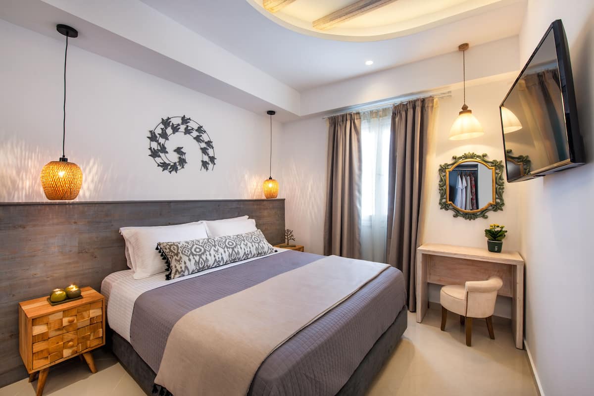 A modern bedroom with a large bed, bedside lamps, a vanity with a mirror, and a flat-screen TV.