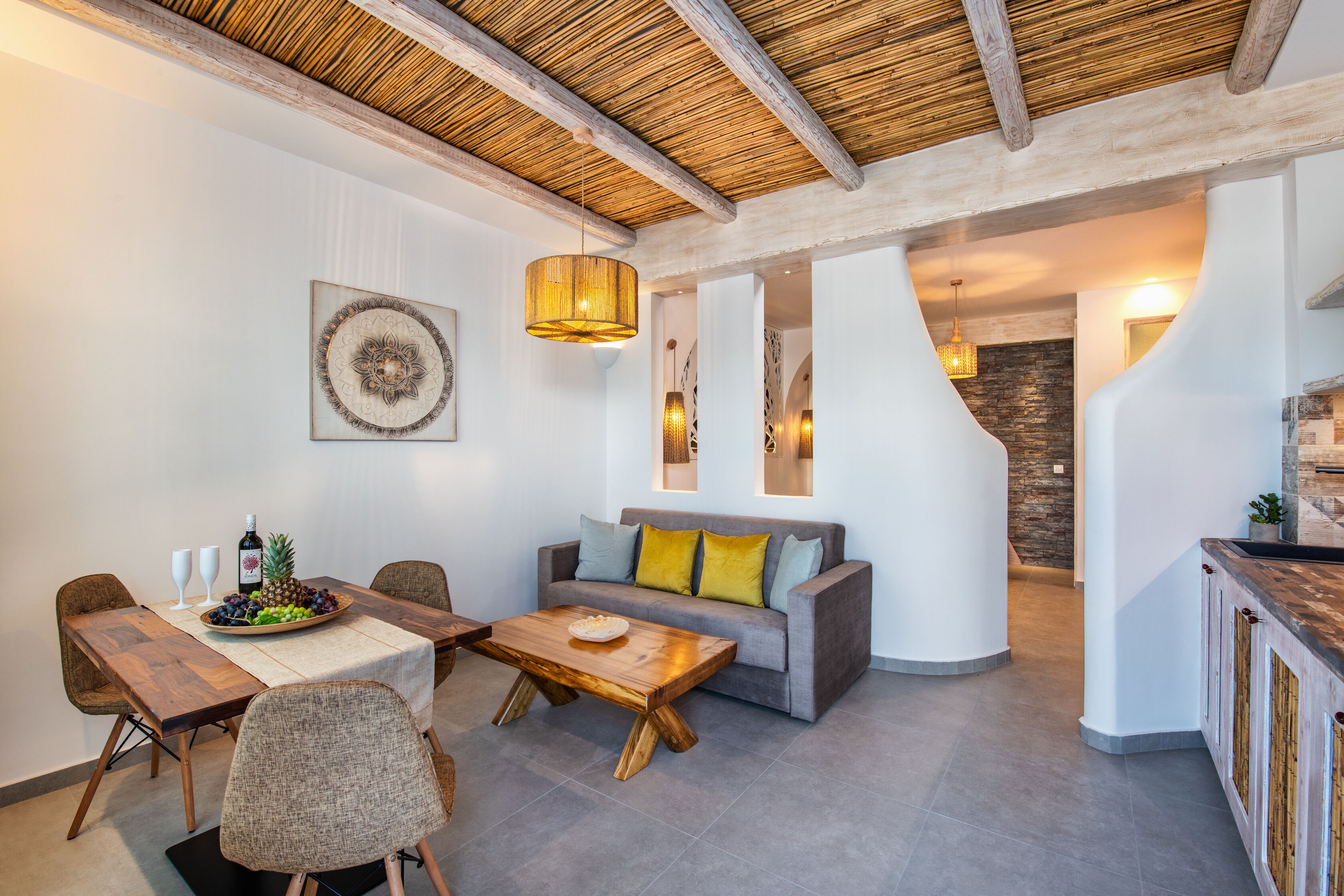 A modern living room with a wooden dining table, sofa, and coffee table. There is a kitchen area with a wooden countertop and cabinets.