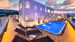 A modern villa with a swimming pool, outdoor seating, and a staircase leading to the upper floor. - Abasa Suites (Santorini)