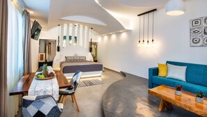A modern living room with a sofa, a dining table with a fruit bowl, and a bed with a view to the dining area. - Abasa Suites (Santorini)