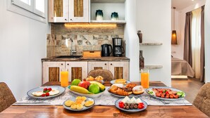A dining table set with various breakfast items, a coffee maker, and a fruit bowl. - Abasa Suites (Santorini)