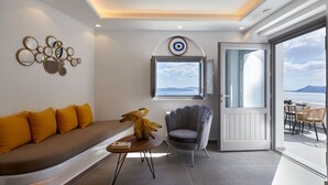 Ein modernes Wohnzimmer mit einer Couch, einem Sessel, einem kleinen Tisch mit einer Vase und einem Fenster mit Meerblick.