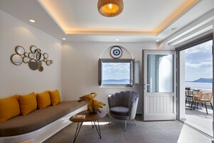Una sala de estar moderna con un sofá, un sillón, una mesita con un florero y un ventanal con vista al mar.