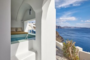 A white-walled room with a view of the sea and a pool. - Allure Breeze Suites (Santorini)