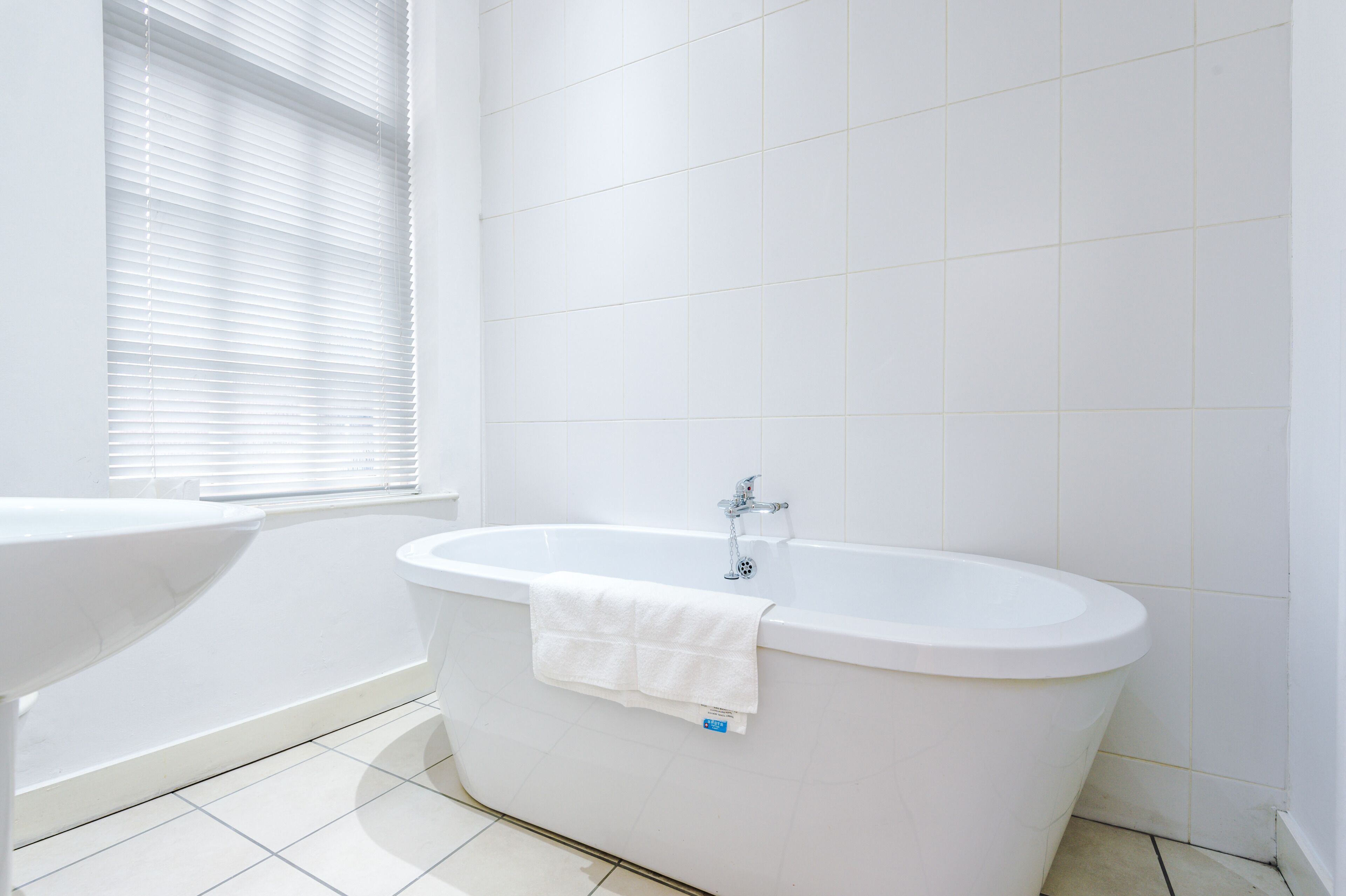 A modern bathroom with a freestanding bathtub, a sink, and a window with blinds.