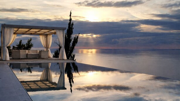 En infinitypool som speglar himlen och ett avskärmat sittområde med utsikt över havet.