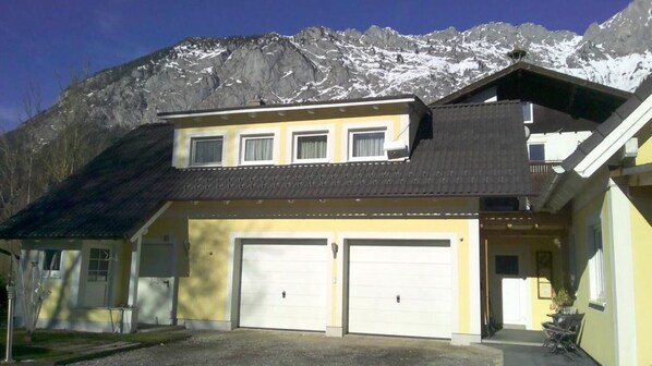 Une maison à deux étages avec un garage, un balcon et une vue sur les montagnes en toile de fond.