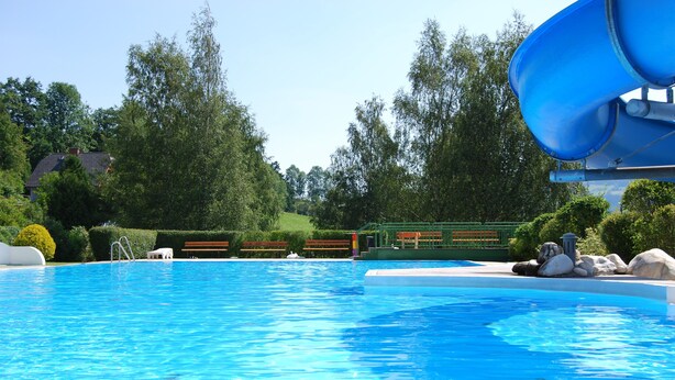 Ein Schwimmbecken mit Wasserrutsche, umgeben von Grünpflanzen und einer Bank.