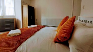 A bedroom with a bed, a radiator, a window with curtains, a wardrobe, and a door. - Belvidere Apartments by Top House (Liverpool)