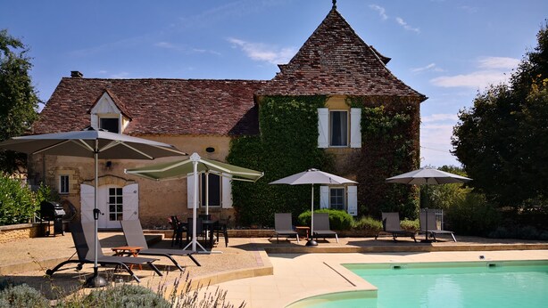 A villa with a swimming pool, outdoor seating, and a garden.