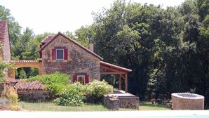 A stone house with a red roof and a pool in the foreground.