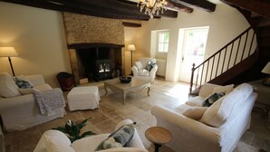 A cozy living room with a fireplace, white sofas, a coffee table, and a staircase.