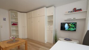 A living room with a wooden table, white cabinets, a TV on a stand, and a bookshelf. - House by the sea14 - App. 071 WB (Sylt)
