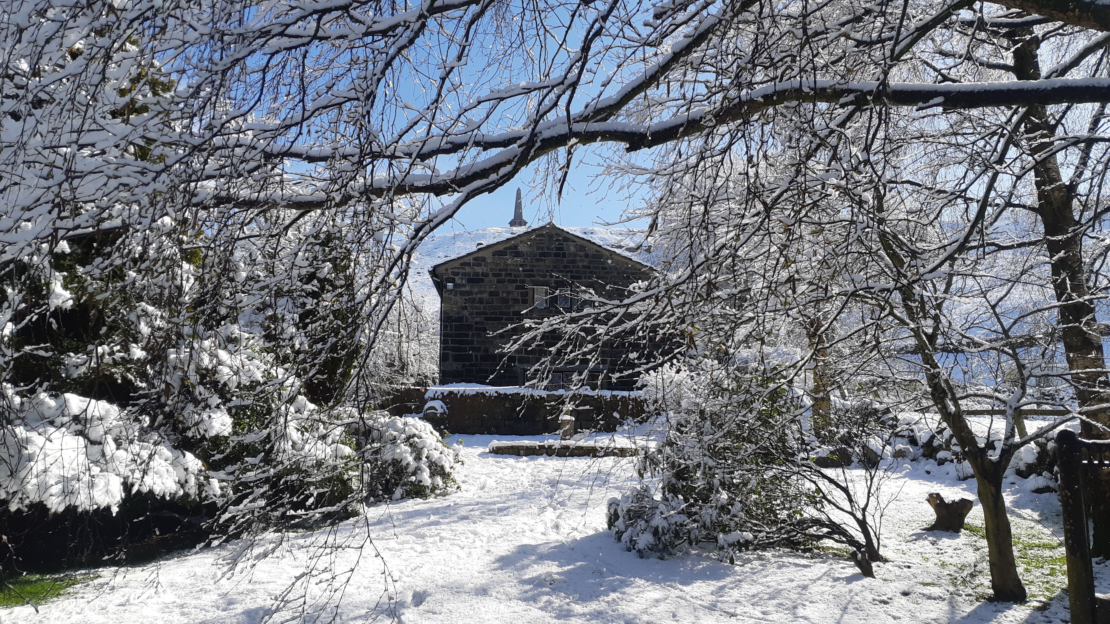 Eine verschneite Landschaft mit einem steinernen Gebäude in der Mitte, umgeben von schneebedeckten Bäumen und Büschen.