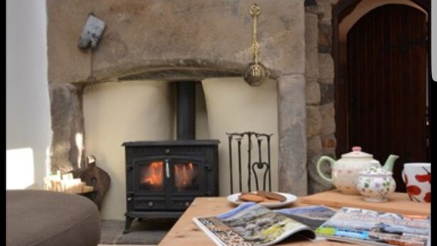 A cozy living room with a stone fireplace, a wooden table with magazines, and a tea set. - Greave Farm Todmorden Tranquil Cottage Retreat (Todmorden)