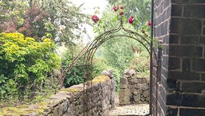 A stone archway leading to a garden with blooming flowers and lush greenery. - Greave Farm Todmorden Tranquil Cottage Retreat (Todmorden)
