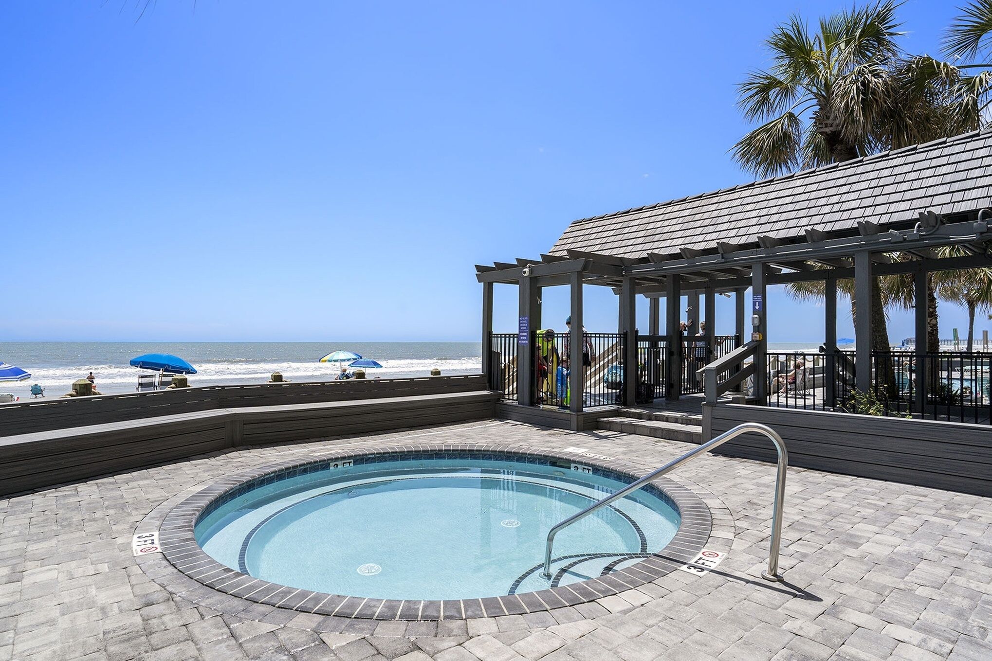 A pool area with a view of the beach, a covered seating area, and a pool with a tiled edge.