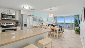 Una cocina con una isla central, un comedor con mesa y sillas, y vista al océano a través de amplios ventanales.
