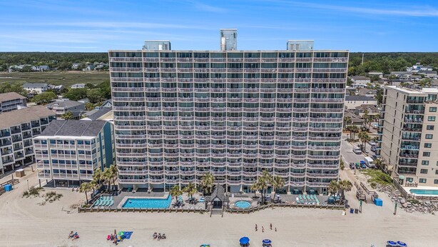 Un hotel de varios pisos con balcones, zona de piscina y acceso directo a la playa.