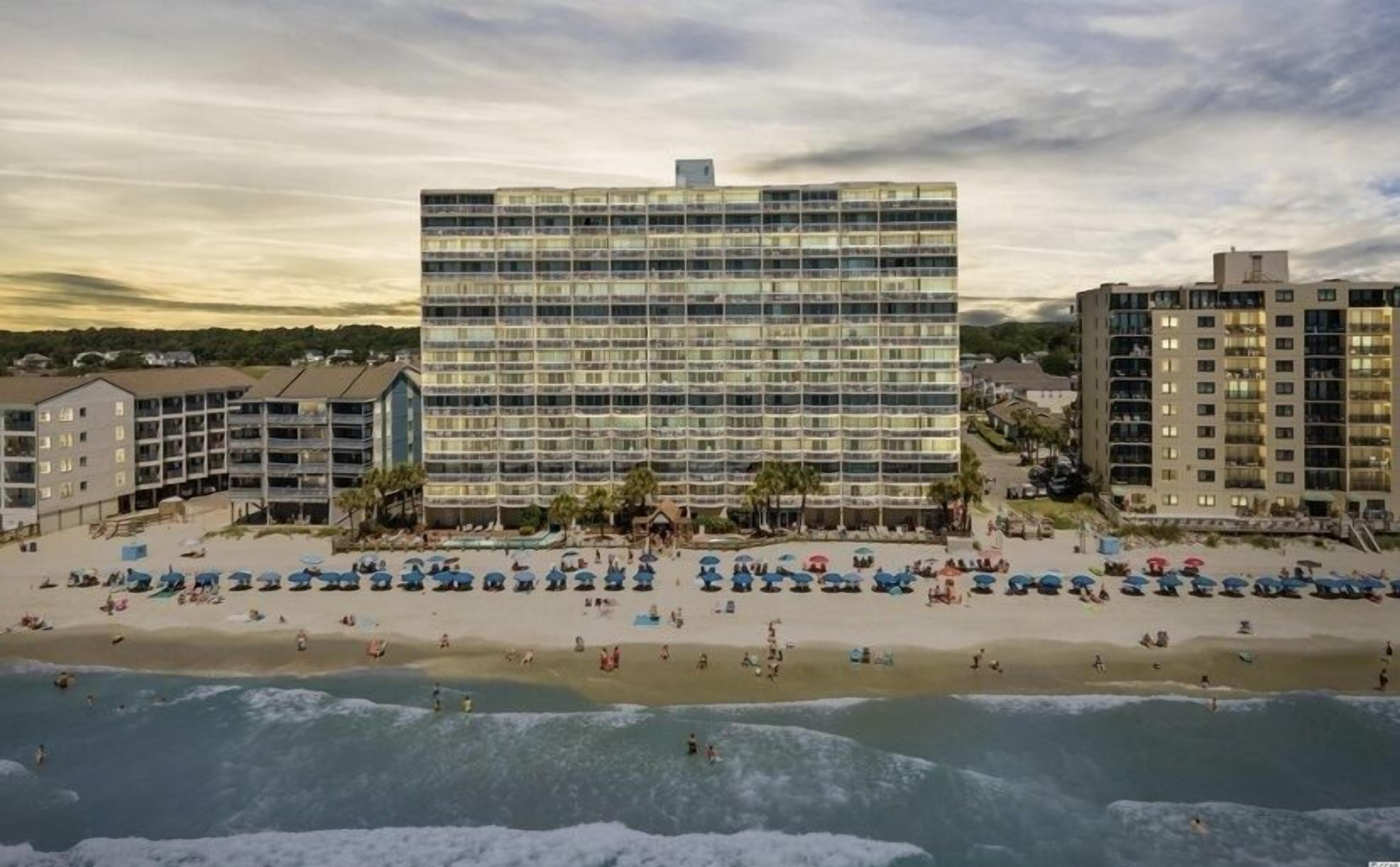 A beachfront hotel with multiple floors, a sandy beach, and ocean waves.