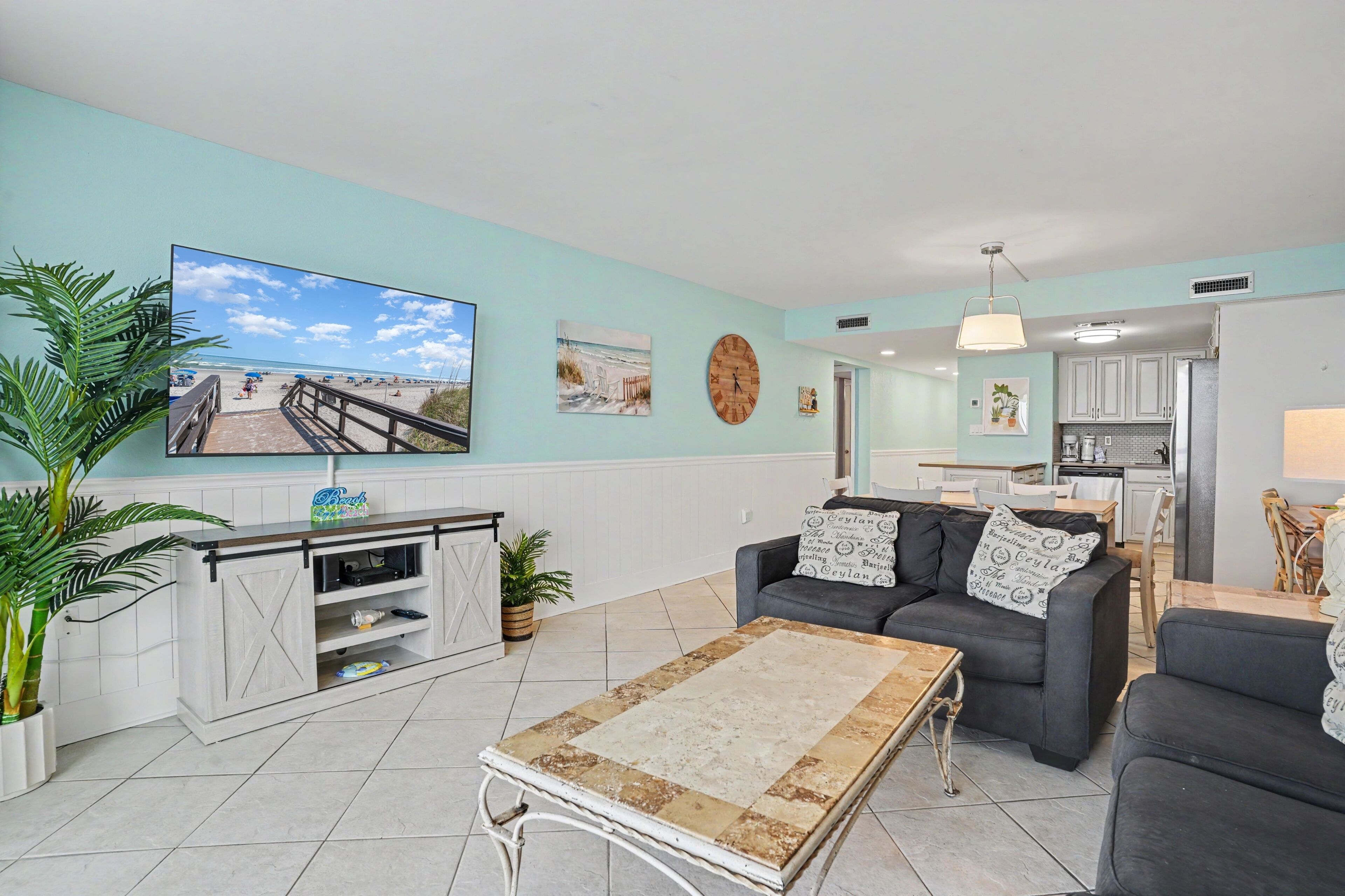 Een woonkamer met een televisie, bank, salontafel en een keuken op de achtergrond.