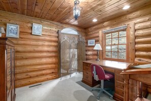 Une chambre aménagée dans un chalet en rondins, avec un bureau en bois, une chaise et une grande fenêtre.